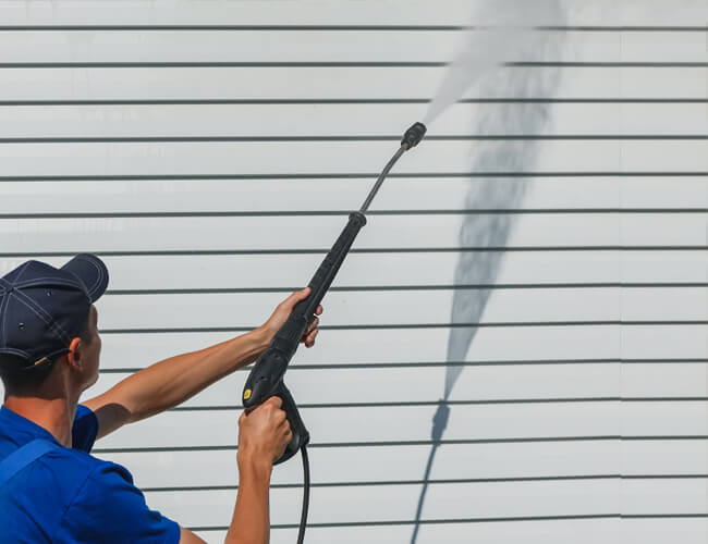 A Diamond Property Wash worker pressure washing the exterior siding of a dirty house outside in the sun.