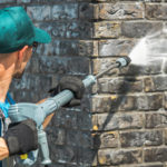 A Diamond Property Wash worker pressure washing a dirty post construction site outside in the sun.